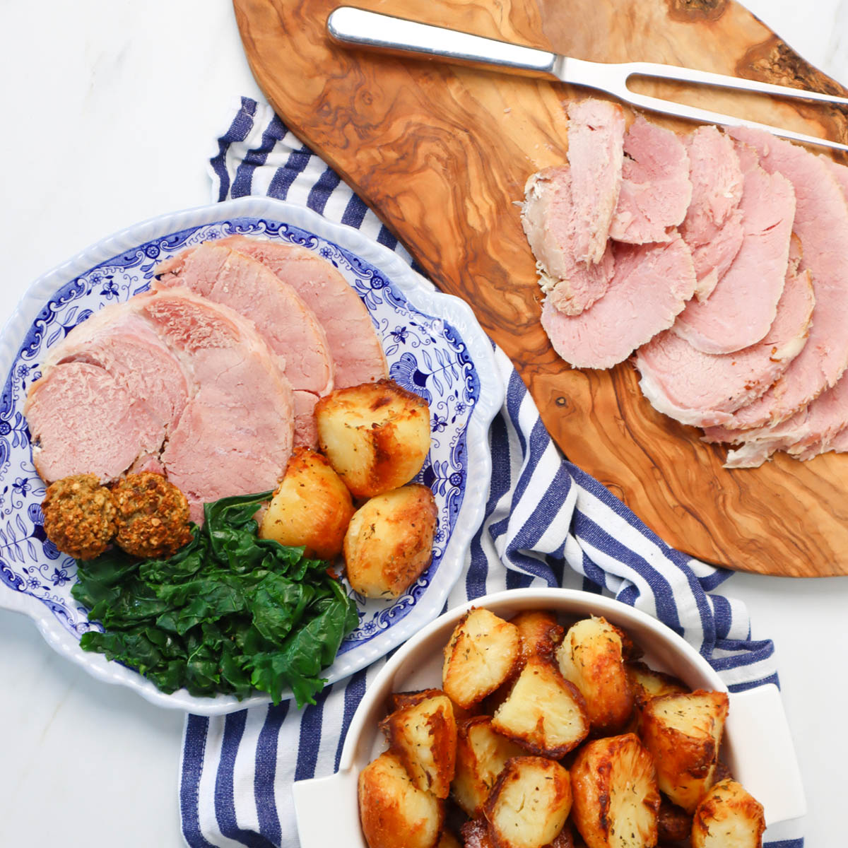 Slow Cooker Ham Sliced slow cooker ham served with roasted potatoes and greens on a blue and white plate.
