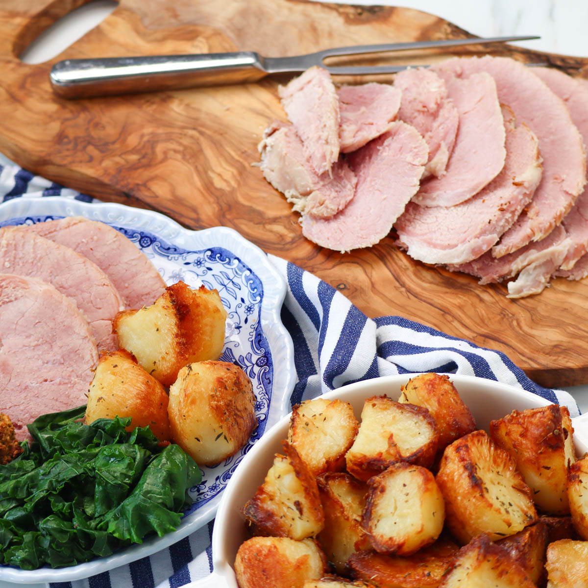 Slow Cooker Ham Sliced slow cooker ham served with crispy roast potatoes and greens on a decorative plate.