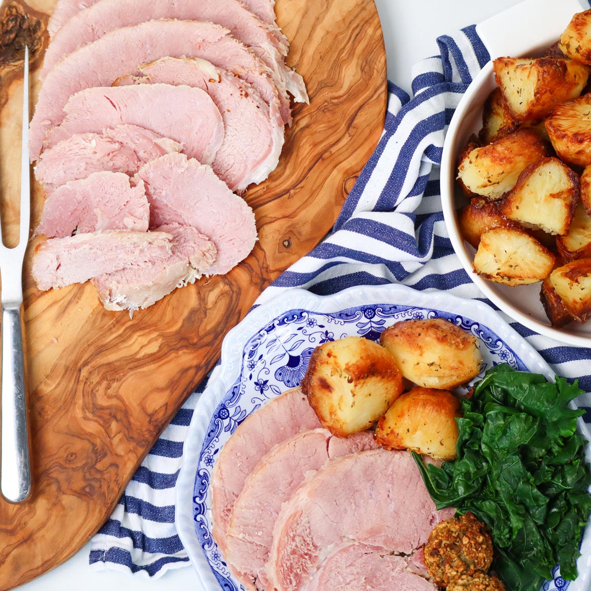 Slow Cooker Ham Sliced slow cooker ham served with roasted potatoes and greens on a wooden board.