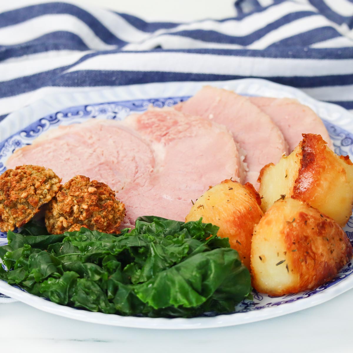 Slow Cooker Ham A plate of slow cooker ham slices with roasted potatoes, greens, and stuffing balls.
